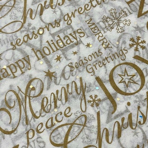 May include: White wrapping paper with gold lettering and accents. The words "Merry Christmas", "Happy Holidays", and "Seasons Greetings" are visible. The design includes stars, snowflakes, and the word "Joy".