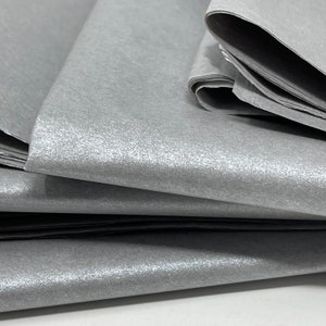 May include: A stack of silver tissue paper with a subtle shimmer. The paper is folded and has a soft, crinkled texture.