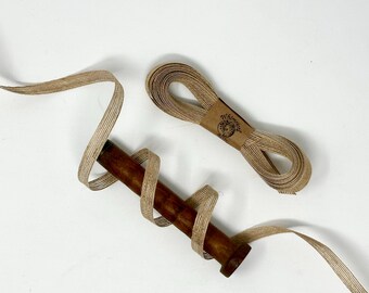 Puede incluir: Un carrete de cinta tejida de color marrón natural con rayas, con un pasador de madera y una etiqueta de papel marrón con el texto "Whimsical"