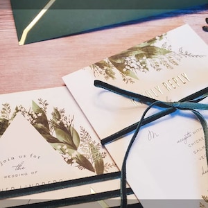 May include: A wedding invitation with a green and white floral design. The invitation is tied with a green velvet ribbon and includes a RSVP card with a list of dinner options.