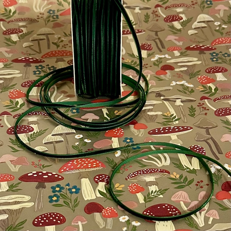 May include: A spool of dark green velvet ribbon on a background of brown wrapping paper with a repeating pattern of mushrooms and flowers.