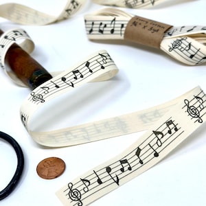 May include: White cotton ribbon with black musical notes printed on it. The ribbon is 1/2 inch wide and 3 yards long. The ribbon is rolled up and tied with a brown paper tag that says "1/2" x 3yd".