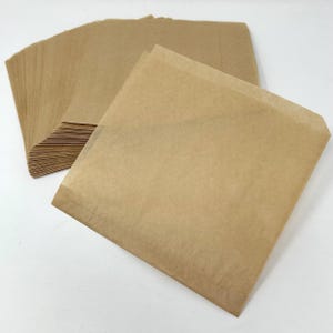 May include: A stack of brown paper bags, with one bag unfolded and lying flat on a white surface.