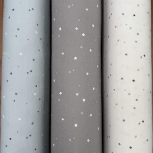 May include: Three rolls of fabric with a white star pattern on a light blue, gray, and white background.
