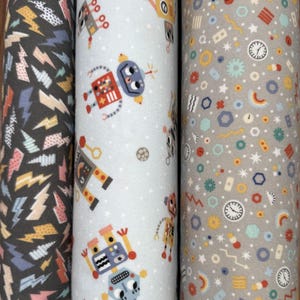 May include: Three rolls of fabric with different patterns. One roll has a dark gray background with colorful lightning bolts. Another has a light blue background with robot illustrations. The third roll has a gray background with clocks, stars, and geometric shapes.