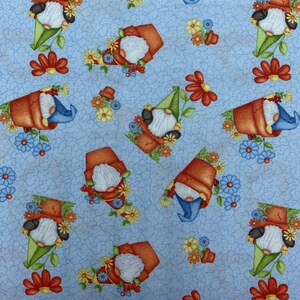 May include: A blue fabric with a repeating pattern of gnomes in flower pots. The gnomes are wearing red hats and have white beards. The flower pots are orange and have green plants growing out of them. The background is a light blue with a subtle texture.