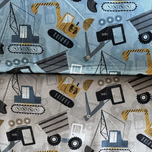 May include: Fabric featuring a repeating pattern of construction vehicles in shades of blue, gray, yellow, and black. The design includes cranes, excavators, dump trucks, and other machinery. The background is a light blue and gray.
