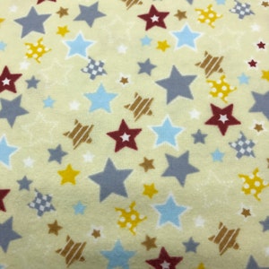 May include: A fabric with a light yellow background, featuring a scattered pattern of stars in various colors and designs. The stars include shades of gray, blue, red, yellow, and brown, with some having striped or dotted patterns.