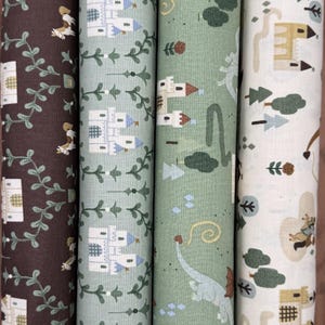May include: Four rolls of fabric with whimsical patterns. Designs include castles, dragons, trees, and knights in shades of brown, green, and white. The fabric is likely cotton or a similar material, suitable for quilting or crafting projects.