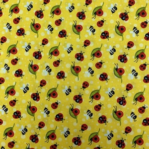 May include: A yellow fabric with a repeating pattern of red ladybugs, bees, and leaves. The ladybugs are in various poses, some with their wings open and some with their wings closed. The bees are all flying and the leaves are green.
