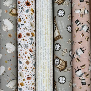 May include: Five rolls of fabric featuring distinct patterns: a gray roll with sheep, a white roll with small orange and blue flowers, a cream roll with printed nursery rhymes, a gray roll with clocks and mice, and a pink roll with figures and cakes.