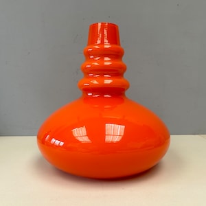 May include: A vibrant orange glass vase with a bulbous base and a cylindrical neck. The vase has a glossy finish and a unique, rounded shape. The neck features a series of horizontal ridges, adding texture to the design. The vase is a decorative item.