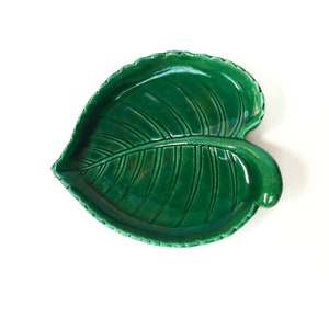 Peut inclure: Un plat en céramique vert émeraude en forme de feuille. Le plat présente des nervures détaillées et un bord festonné, parfait pour servir ou décorer. Le design évoque la nature et ajoute une touche d'élégance.
