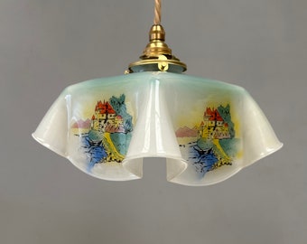 May include: A white glass pendant light fixture with a ruffled edge and a painted scene of a castle and a lake. The fixture has a brass chain and a brass canopy.