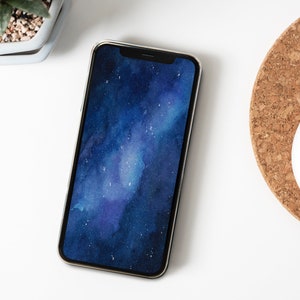 Op de afbeelding: Een smartphone met een donkerblauwe en paarse sterrenstelsel-achtergrond op het scherm. Het apparaat heeft een slank metalen frame en een zwarte inkeping aan de bovenkant van het display, met een levendig kosmisch patroon met witte stippen.