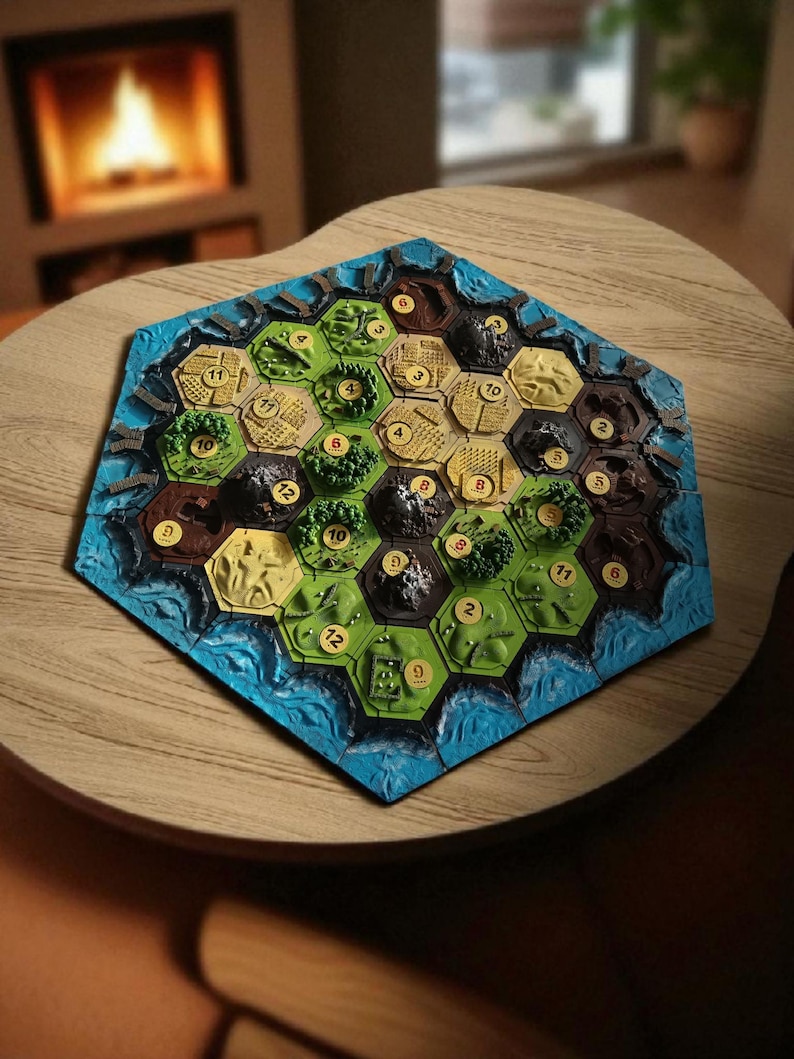 May include: A hexagonal board game with terrain tiles, including green fields, brown mountains, and blue water. The game board is set on a wooden table, with a fireplace in the background. The tiles have numbers.