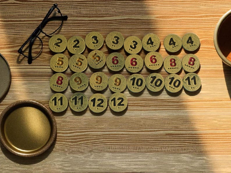 May include: A collection of small, round, antique-style game tokens with numbers from 2 to 12. The tokens are arranged on a wooden surface, with a pair of eyeglasses and a small brass tray visible.