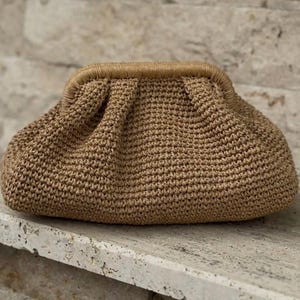 May include: A brown crocheted clutch bag with a gathered design. The bag has a brown leather trim.
