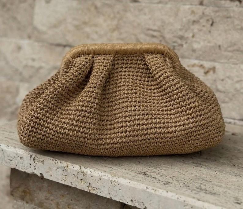 May include: A brown crocheted clutch bag with a gathered design. The bag has a brown leather trim.