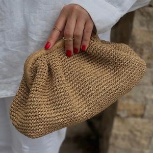 May include: A tan crocheted clutch bag with a slightly rounded shape.