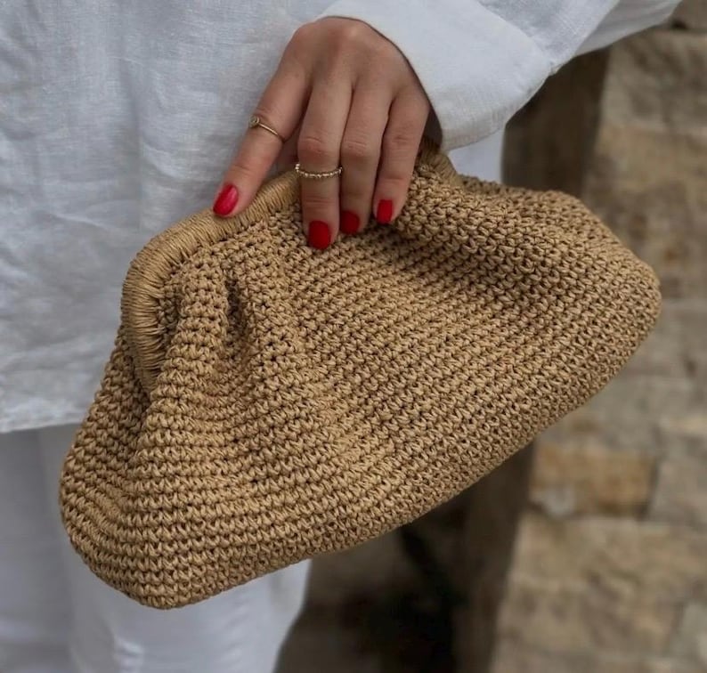 May include: A tan crocheted clutch bag with a slightly rounded shape.