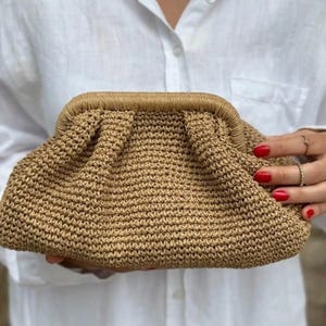 May include: A tan crocheted clutch bag with a gathered top and a brown trim.