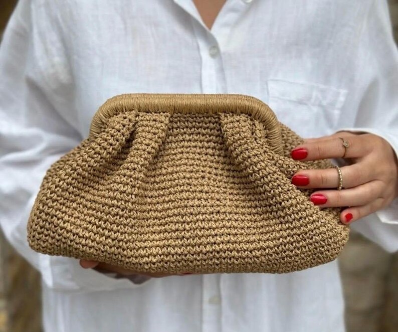 May include: A tan crocheted clutch bag with a gathered top and a brown trim.