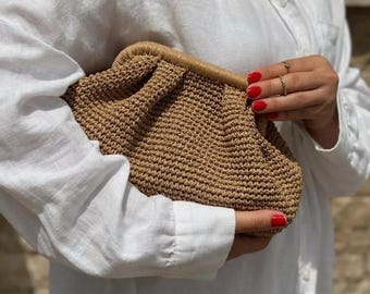 Puede incluir: Un bolso de mano tejido marrón con un diseño fruncido. El bolso se sostiene en una mano con esmalte de uñas rojo.