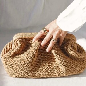 May include: A brown woven clutch bag with a textured surface. The bag is made of a tightly woven material and has a slightly rounded shape.