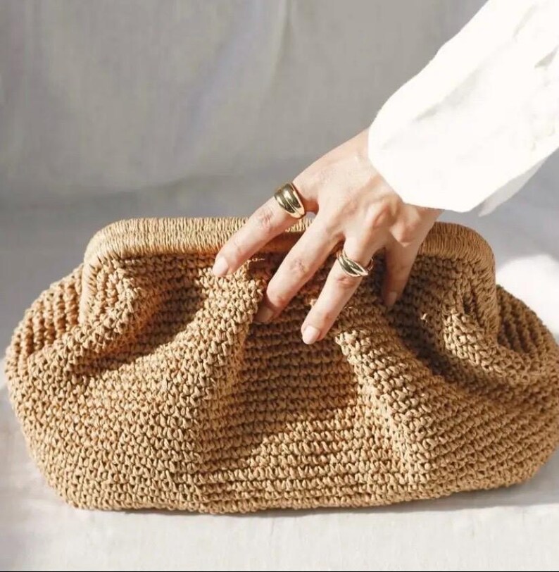 May include: A brown woven clutch bag with a textured surface. The bag is made of a tightly woven material and has a slightly rounded shape.
