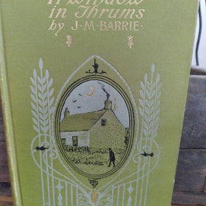 May include: A green book cover with gold lettering that reads "A Window in Thrums by J.M. Barrie". The cover features a black and white illustration of a house with a crescent moon in the sky.