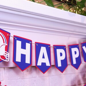 May include: A blue and red banner with white letters spelling "HAPPY" and a football helmet with a buffalo silhouette. The banner is strung with twine.