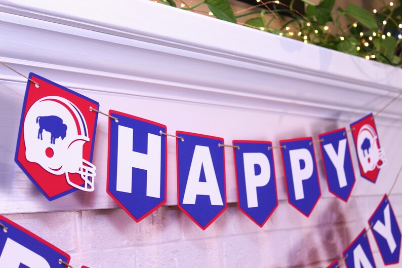 May include: A blue and red banner with white letters spelling "HAPPY" and a football helmet with a buffalo silhouette. The banner is strung with twine.