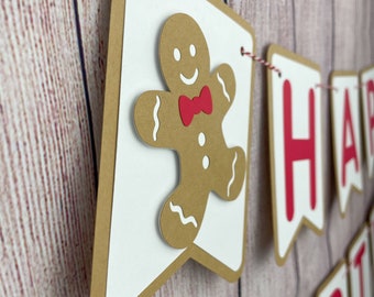May include: A gingerbread man banner with the words "Happy Birthday" in red letters. The banner is made of brown and white cardstock and is strung together with red and white twine.