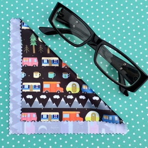 May include: A black microfiber cleaning cloth with a colorful pattern of camper vans, mountains, and trees. The cloth is folded in a triangle shape and a pair of black eyeglasses are lying on top of it.
