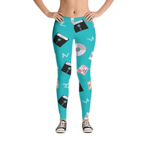 Può includere: Un paio di leggings blu turchese con un motivo di floppy disk, CD e file di computer. I leggings sono su uno sfondo bianco.