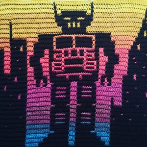 May include: A crocheted blanket with a pixelated robot design in black yarn against a gradient background of yellow, orange, pink, blue, and purple.