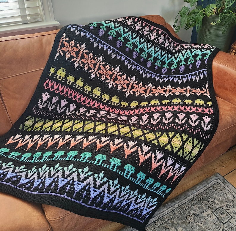 K&ouml;nnte beinhalten: Eine schwarze und wei&szlig;e H&auml;keldecke mit einem bunten geometrischen Muster. Die Decke zeigt eine Vielzahl von Pastellfarben, darunter Rosa, Blau, Gr&uuml;n und Gelb. Die Decke ist aus einem weichen, strukturierten Garn gefertigt und hat einen Fransenrand.