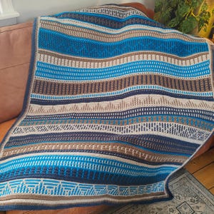 May include: A crocheted throw blanket with a striped pattern in shades of blue, brown, and white.
