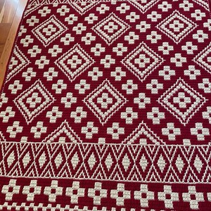 May include: A red and cream crochet rug with a geometric pattern. The rug has a diamond pattern with a flower design in the center of each diamond.