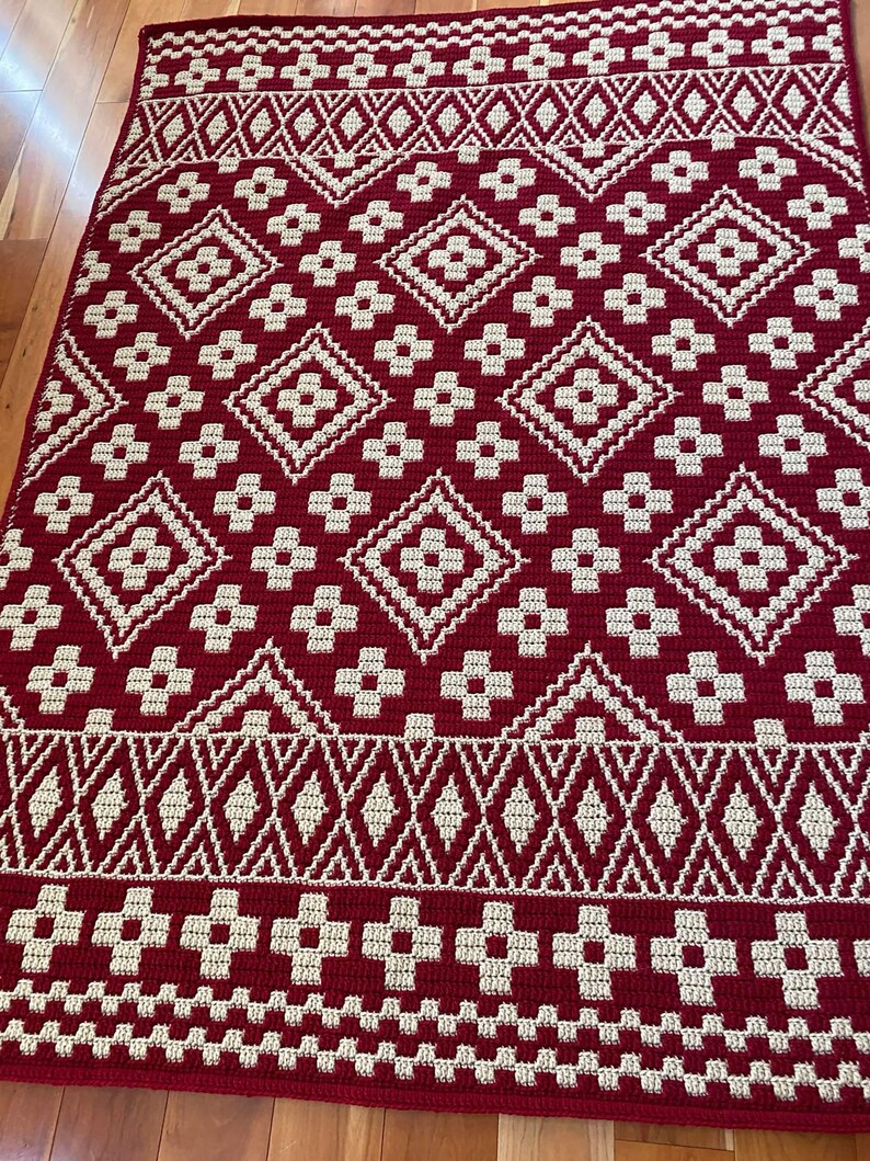 May include: A red and cream crochet rug with a geometric pattern. The rug has a diamond pattern with a flower design in the center of each diamond.