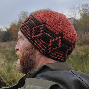 May include: A man wearing a brown and black crocheted beanie with a geometric pattern. The beanie is worn on his head and covers his ears. He is wearing a green jacket.