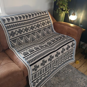 Może przedstawiać: Czarno-biały koc z geometrycznym wzorem, z niebieskimi akcentami i żółtymi frędzlami. Koc jest zarzucony na brązową skórzaną sofę.