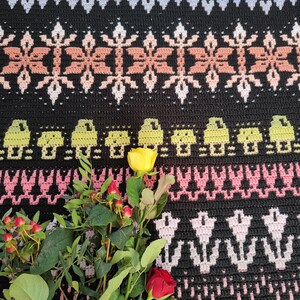 K&ouml;nnte beinhalten: Ein Strau&szlig; gelber und roter Rosen mit gr&uuml;nen Bl&auml;ttern auf einer schwarz-wei&szlig;en H&auml;keldecke mit geometrischem Muster.