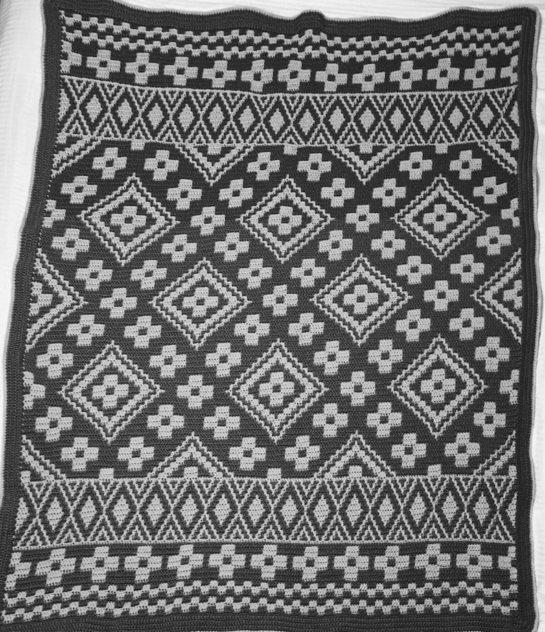 May include: A black and gray crocheted blanket with a geometric pattern. The blanket has a diamond pattern with smaller flower-like shapes in the center of each diamond.