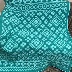 May include: A green and light blue crocheted throw blanket with a geometric pattern. The blanket is made with a repeating diamond and flower design.