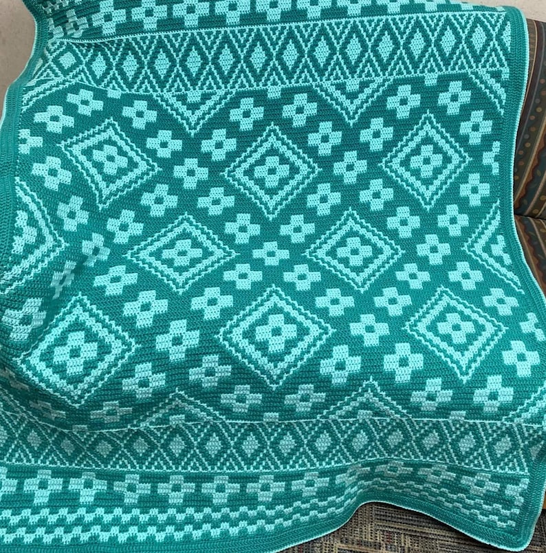 May include: A green and light blue crocheted throw blanket with a geometric pattern. The blanket is made with a repeating diamond and flower design.