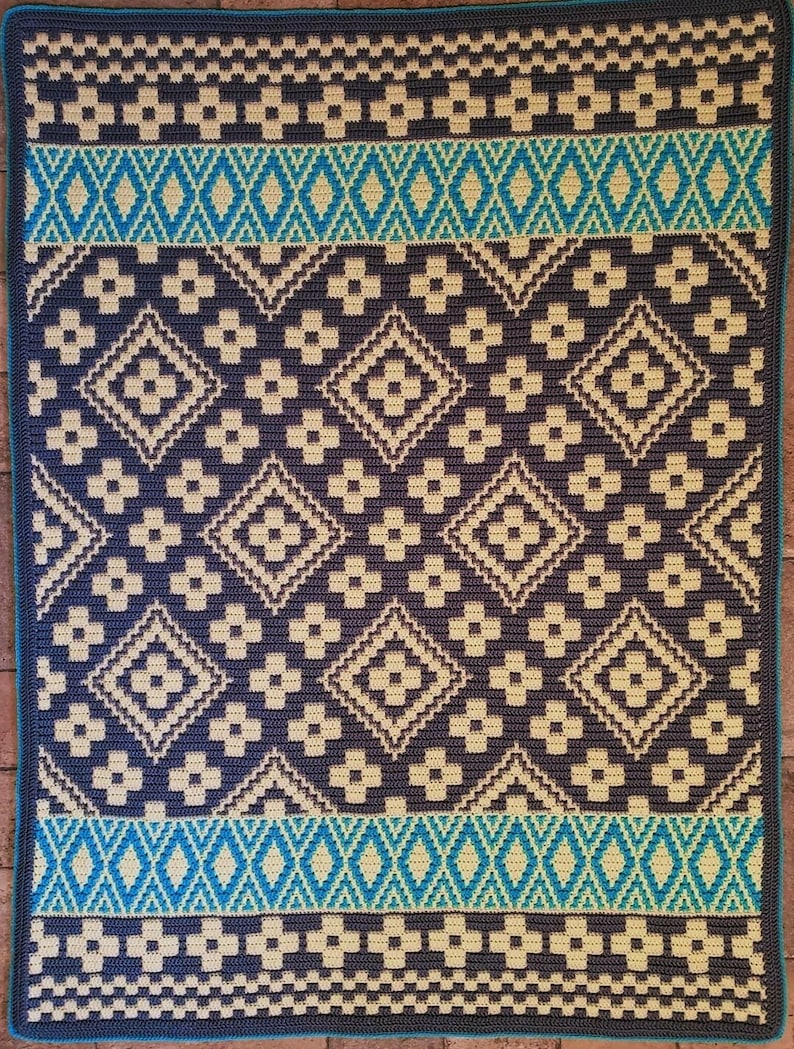 May include: A crocheted rug with a geometric pattern in shades of beige, gray, and blue. The rug has a border of blue and white.