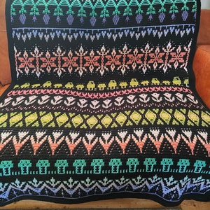 K&ouml;nnte beinhalten: Eine schwarze und wei&szlig;e H&auml;keldecke mit einem farbenfrohen geometrischen Muster. Das Muster zeigt Blumen, Bl&auml;tter und andere abstrakte Formen. Die Decke ist aus verschiedenen farbigen Garnen gefertigt.