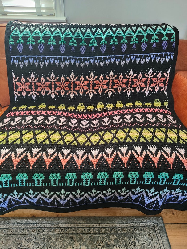 K&ouml;nnte beinhalten: Eine schwarze und wei&szlig;e H&auml;keldecke mit einem farbenfrohen geometrischen Muster. Das Muster zeigt Blumen, Bl&auml;tter und andere abstrakte Formen. Die Decke ist aus verschiedenen farbigen Garnen gefertigt.